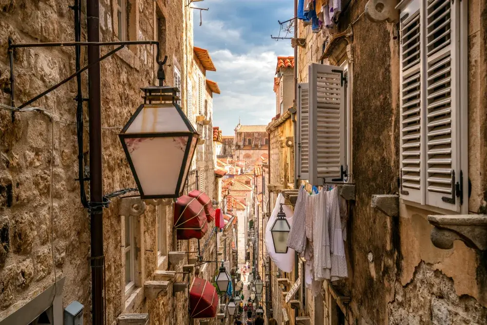 View of a narrow alley on a pleasant day with light fixtures, clothes lines, and awnings in view during the least busy time to visit Dubrovnik