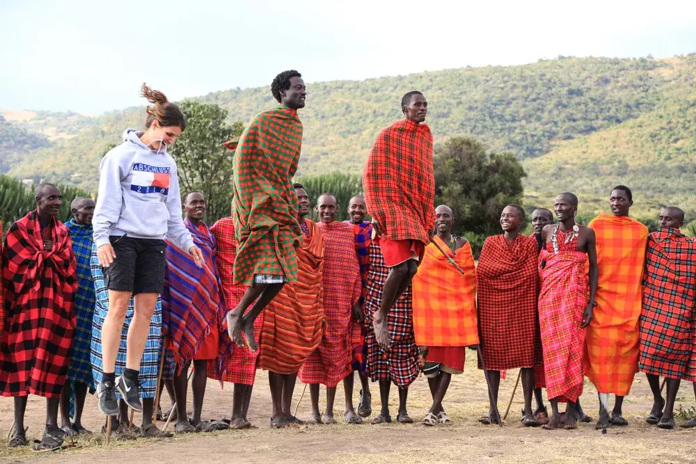 Woman in Hilfiger gear jumping with the Masai Mara tribe