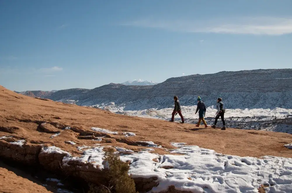 Three tourists walking along a rock face during the winter, the overall cheapest time to visit Moab
