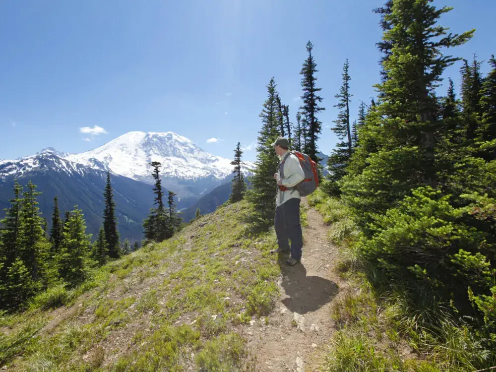 Guy hiking during the best time to visit Seattle with Mount Rainier in the background peaking over the other hills