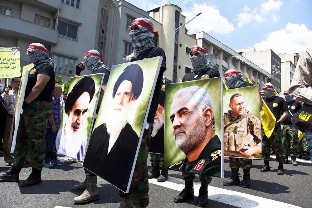 Iranians marching through the streets holding photos of dead military leaders to illustrate that Iran is not safe to visit