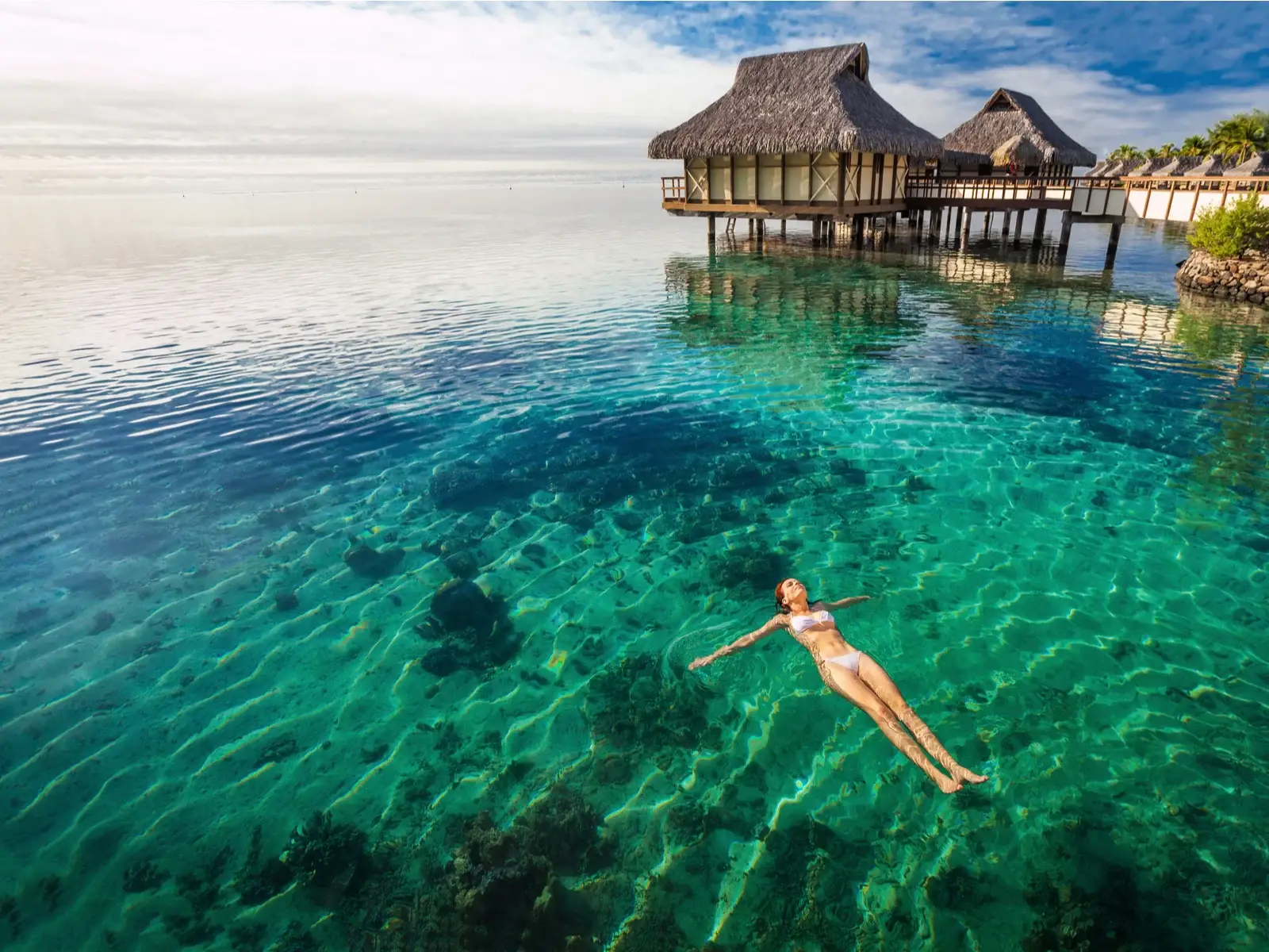 Woman floating on her back in clear green water on a sunny day during the best time to visit Tahiti