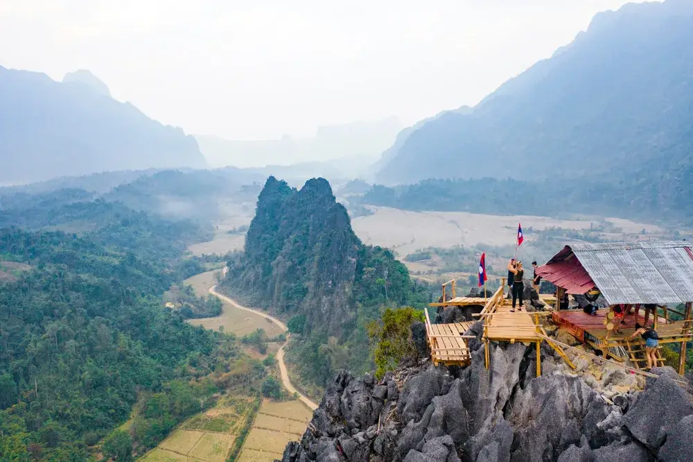 Hikers climbing a wooden tower built on a rock formation during the best time to visit Laos
