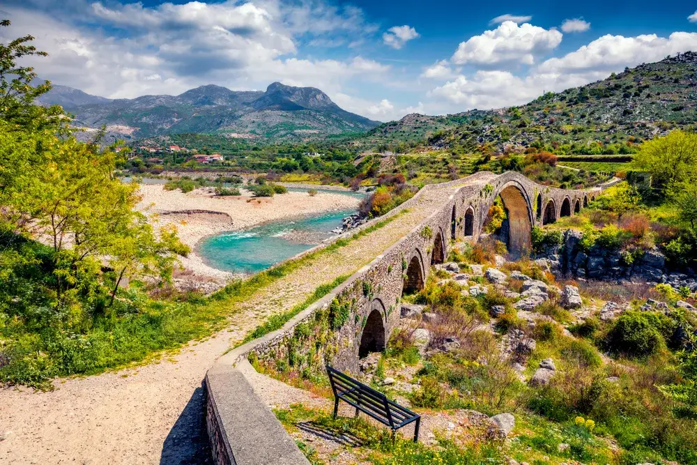 Old Mes Bridge in Shkoder during summer, the best time to visit Albania with clouds overhead and greenery