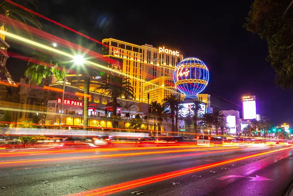 Image of the Vegas Strip pictured at night in a low-exposure shot with cars going by for a guide titled Is Las Vegas Safe to Visit