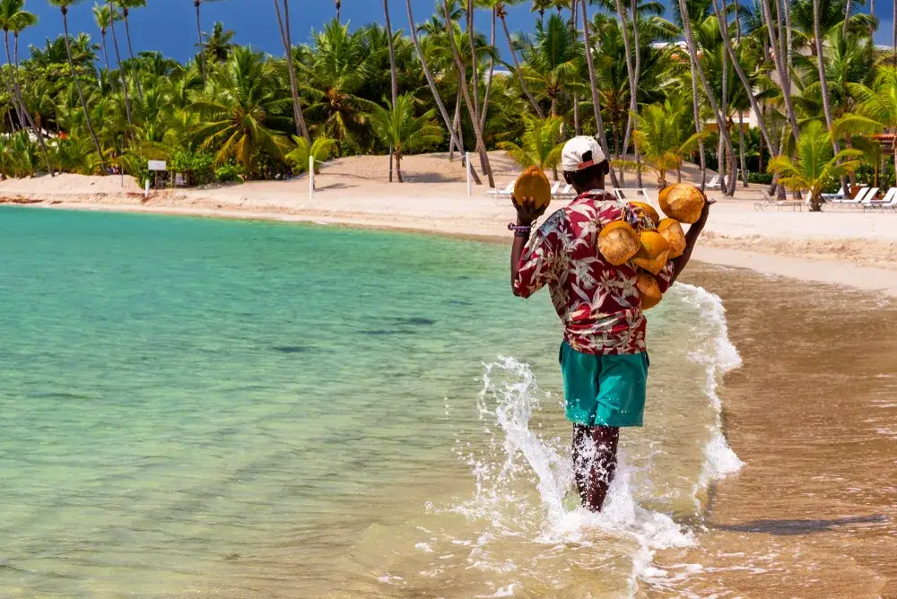 Guy selling coconuts walking along the beach during the best time to visit the Dominican Republic