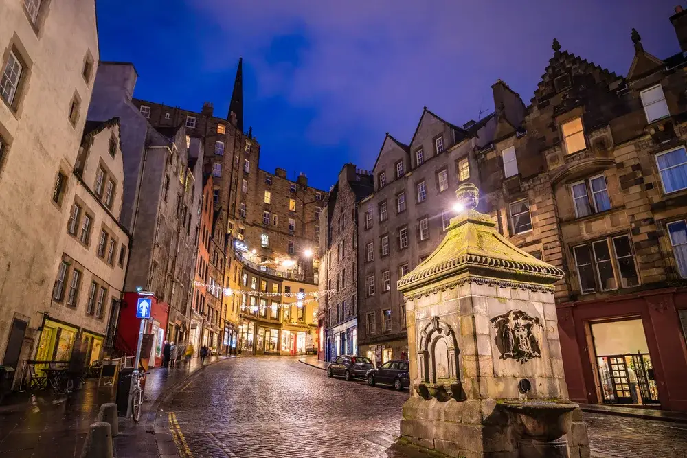 Street view from the perspective of a person walking along the cobblestone path with a cloudy sky above for a piece on the cheapest time to visit Edinburgh