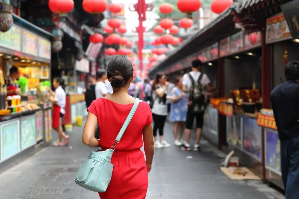 Asian tourist in a red dress walking around in an open-air market to illustrate that China is safe to visit