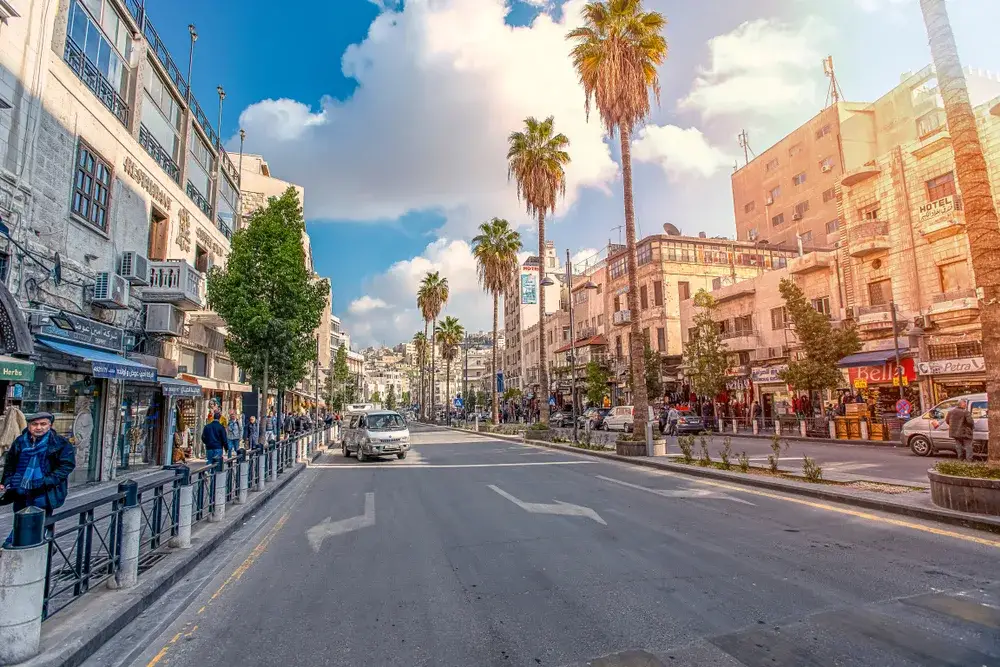 Photo of an empty street in Amman during the least busy time to visit Jordan with trees and neat stone buildings on either side of the street