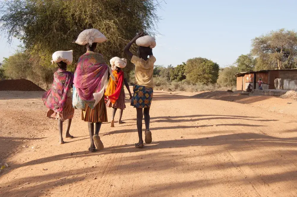 Kids walking down the street with sacks on their heads wearing traditional African clothing on a clear day and walking on a dirt road in a village during the best time to go to Uganda