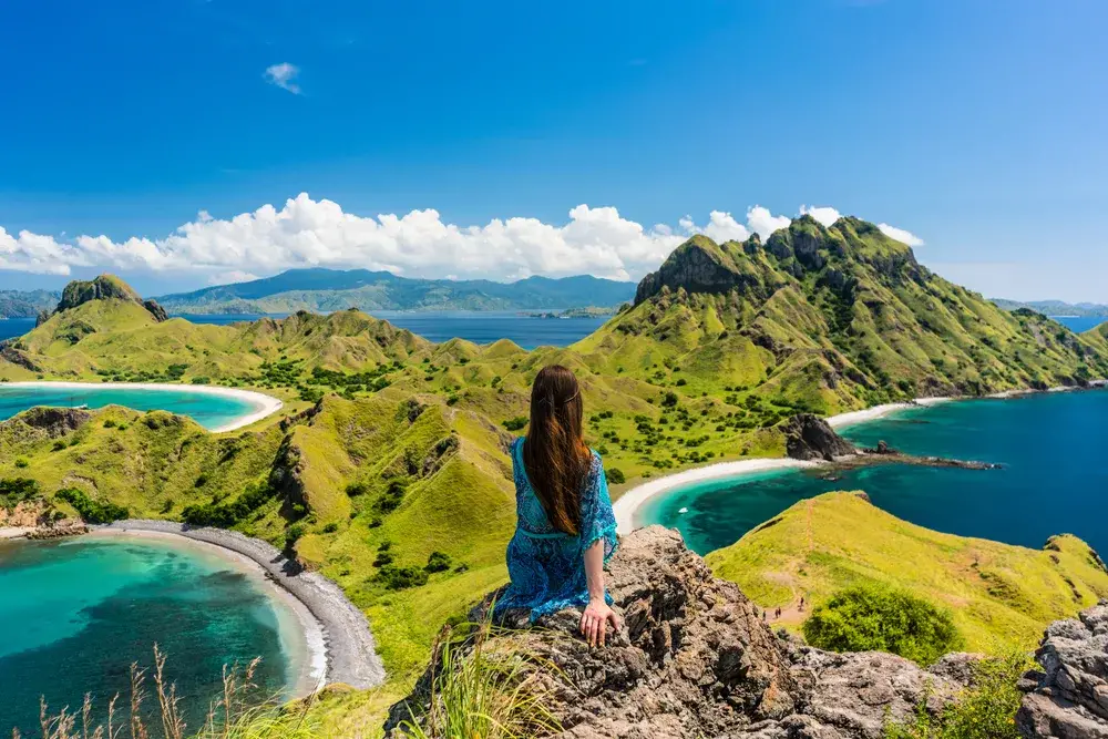 Young woman sitting on rocks overlooking the green mountains on Padar Island during the least busy time to visit Indonesia