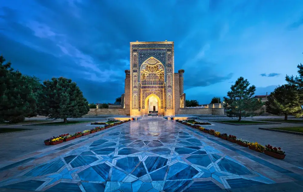 Entrance to Gur-e-Amir with blue walls and a gorgeous tiled courtyard pictured lit up at night