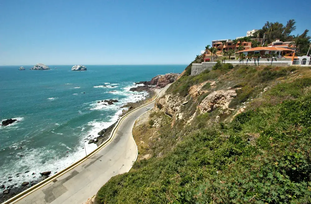 Road winding along the rocky shoreline of the ocean with rock formations jutting out of the water in the distance during the least busy time to visit Mazatlan