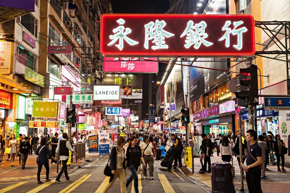 Busy commercial street in Hong Kong pictured for a piece titled Is China Safe to Visit with many people walking around below the bright billboards