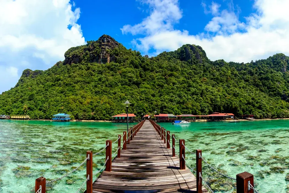 Wooden dock extends into green waters around coral reefs on an island during the least busy time to visit Malaysia