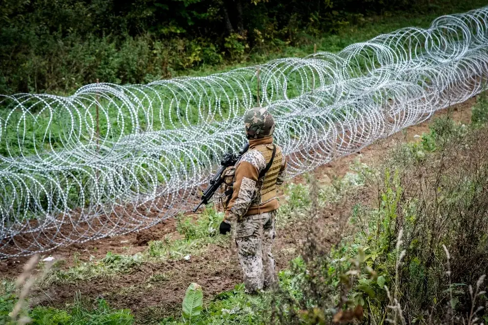 Guard stands at the border of Latvia and Belarus with barbed wire in front of him