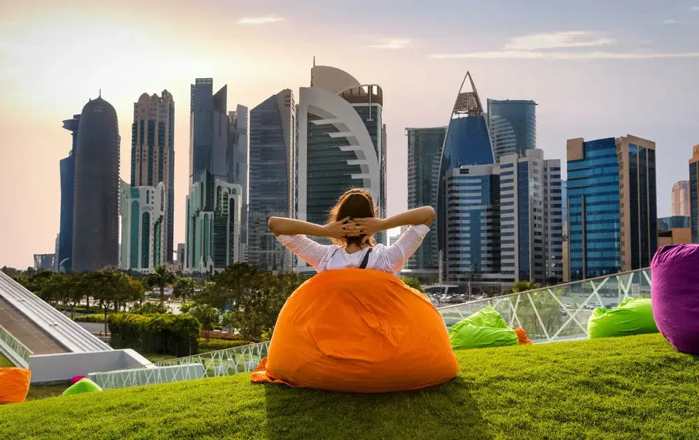 Woman sitting on a bean bag in a park watching the skyline of Doha for a piece on Is Qatar Safe to Visit