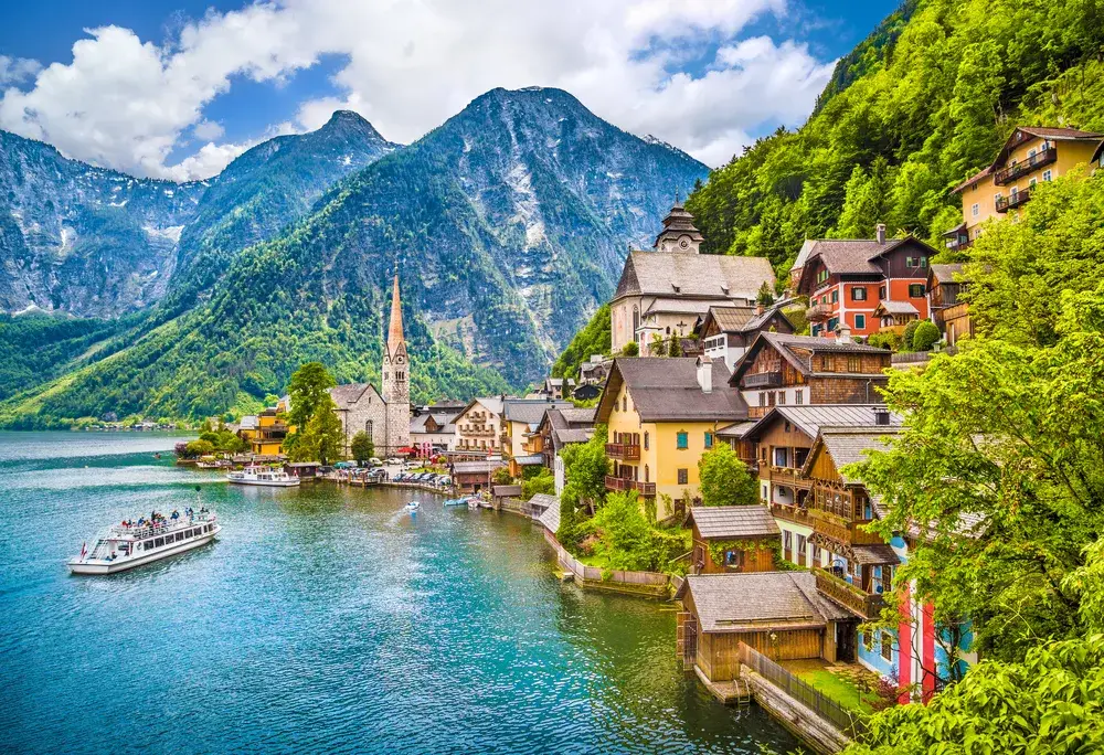Scenic view of the Alps town of Hallstatt with a boat driving by and gorgeous homes and buildings on the hillside