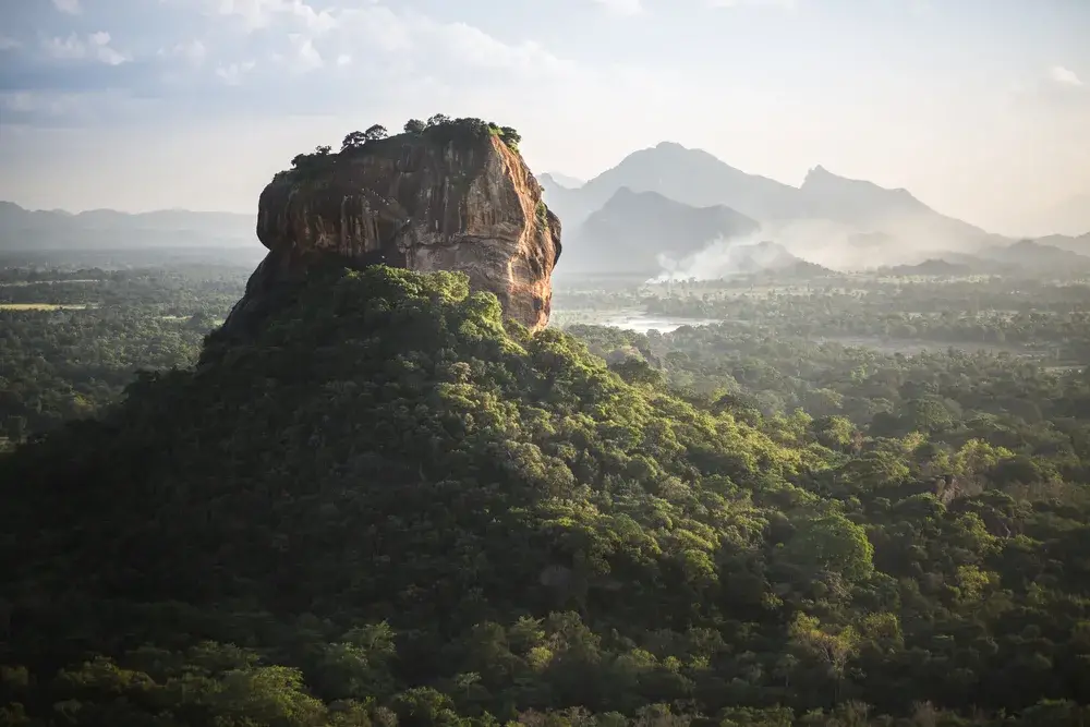 Aerial view of the Sigiriya Lion Rock fortress and surrounding forest during the cheapest time to visit Sri Lanka with fog over the forest