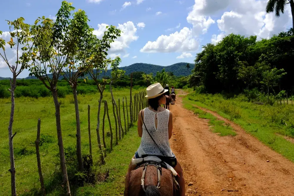 Back view of tourist riding horse on dirt path outside Trinidad to indicate the best time to visit Cuba