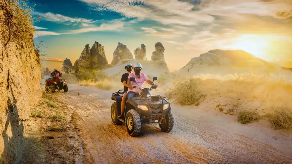 Man and woman on ATVs in the desert with the sun setting over the hill with scorching-hot temperatures during the worst time to visit Cappadocia