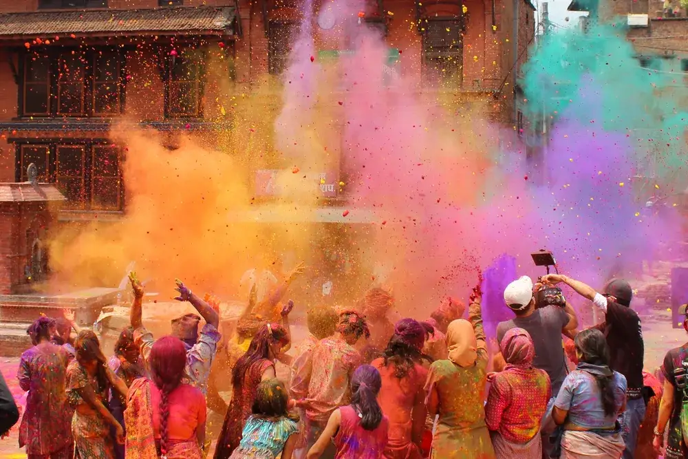 Celebration of color as seen from the street with people throwing colored chalk in the air in front of a temple